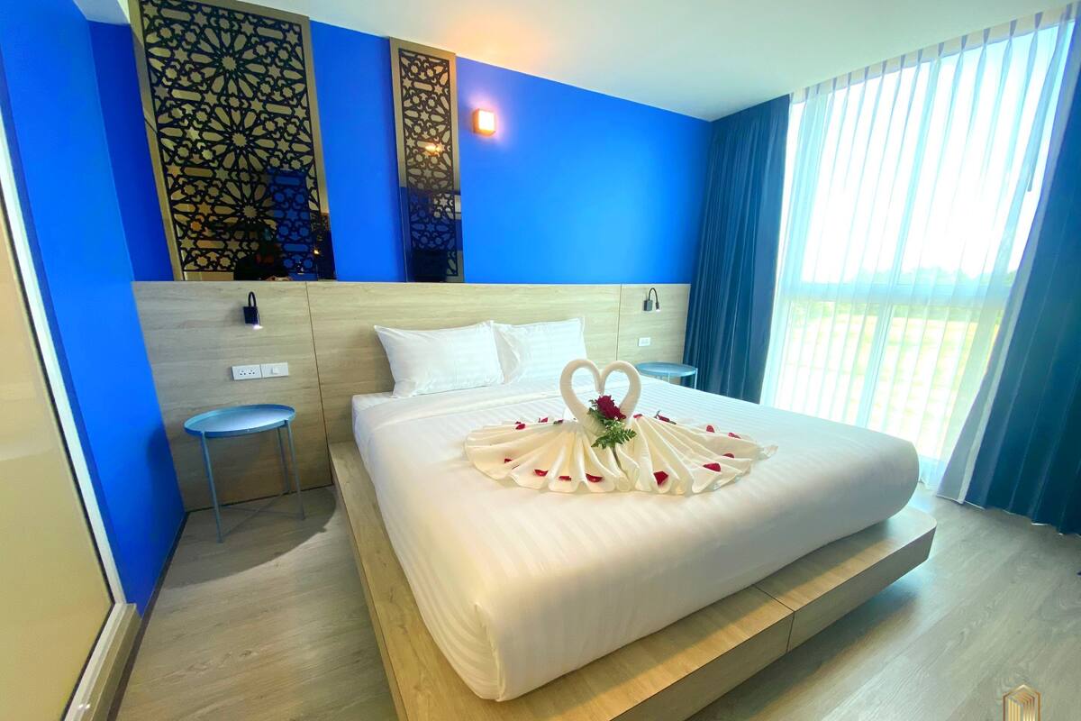 Una habitación de hotel con una cama grande, cabecera de madera, una mesita y un panel decorativo en la pared.