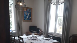 A dining area with a table set for four, two pendant lights, a painting on the wall, and a window with curtains.
