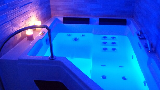 A modern bathtub with a control panel, surrounded by a tiled wall.