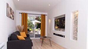 A modern living room with a sofa, a TV mounted on a stone wall, and a sliding glass door leading to an outdoor patio.