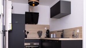 A modern kitchen with black cabinetry, a built-in oven, a coffee machine, and a hanging light fixture.