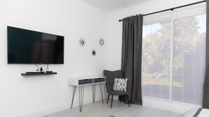 A modern living room with a flat-screen TV, a white console table, a grey armchair, and a large sliding glass door to a garden.