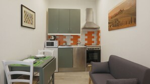 A compact kitchen with a microwave, stove, and cabinets, a dining table with chairs, and a gray sofa. - SweetLittleHouse47: a few steps from the city center (Siena)