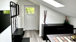 Een moderne, minimalistische kamer met een schuine kap, een zwart bureau, een zwarte bank, een aan de muur bevestigde televisie en een deur die naar buiten leidt.