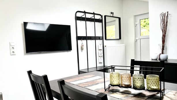 Een moderne keuken met een flatscreen televisie, een zwart metalen rek en een eettafel met stoelen.