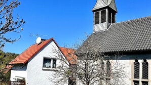 Een traditioneel gebouw met een rood pannendak, een klokkentoren en een klein aangrenzend gebouwtje met een witte gevel.