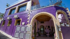 Un immeuble de deux étages, à la façade violette, doté d’un balcon et d’une entrée couverte en forme d’arc.