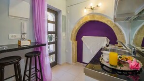 Une cuisine avec un tabouret de bar, une arche violette, un évier et un plateau de petit-déjeuner avec du jus d’orange.