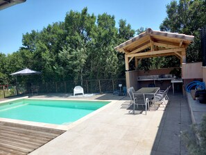 A pool area with a wooden pergola, a barbecue station, and a covered seating area.