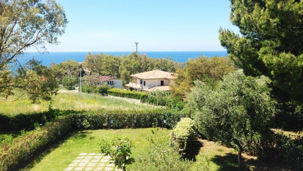 A coastal property with a view of the sea, surrounded by greenery and a few buildings.