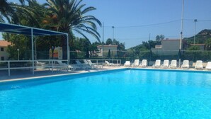 A swimming pool with white lounge chairs and a covered area.