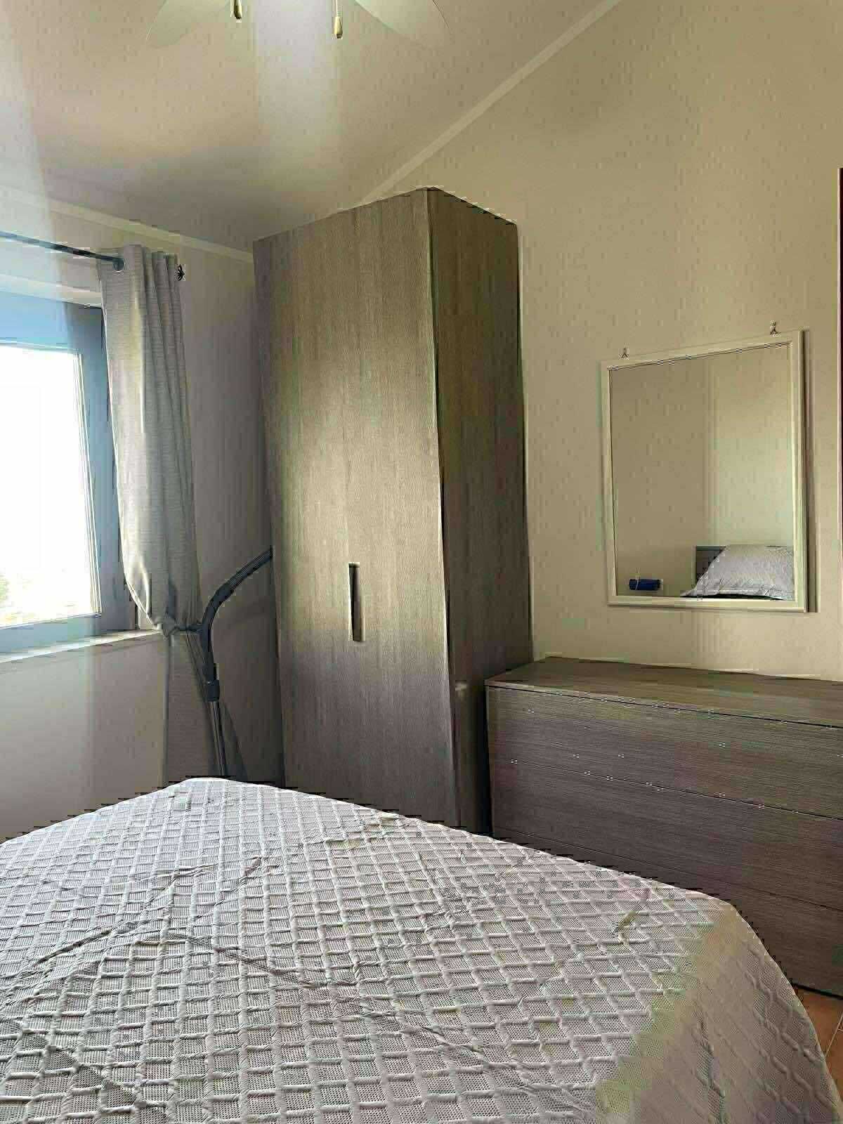 A bedroom with a bed, a wardrobe, a mirror, and a window with curtains.