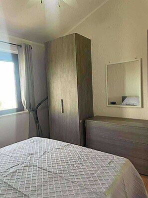 A bedroom with a bed, a wardrobe, a mirror, and a window with curtains.
