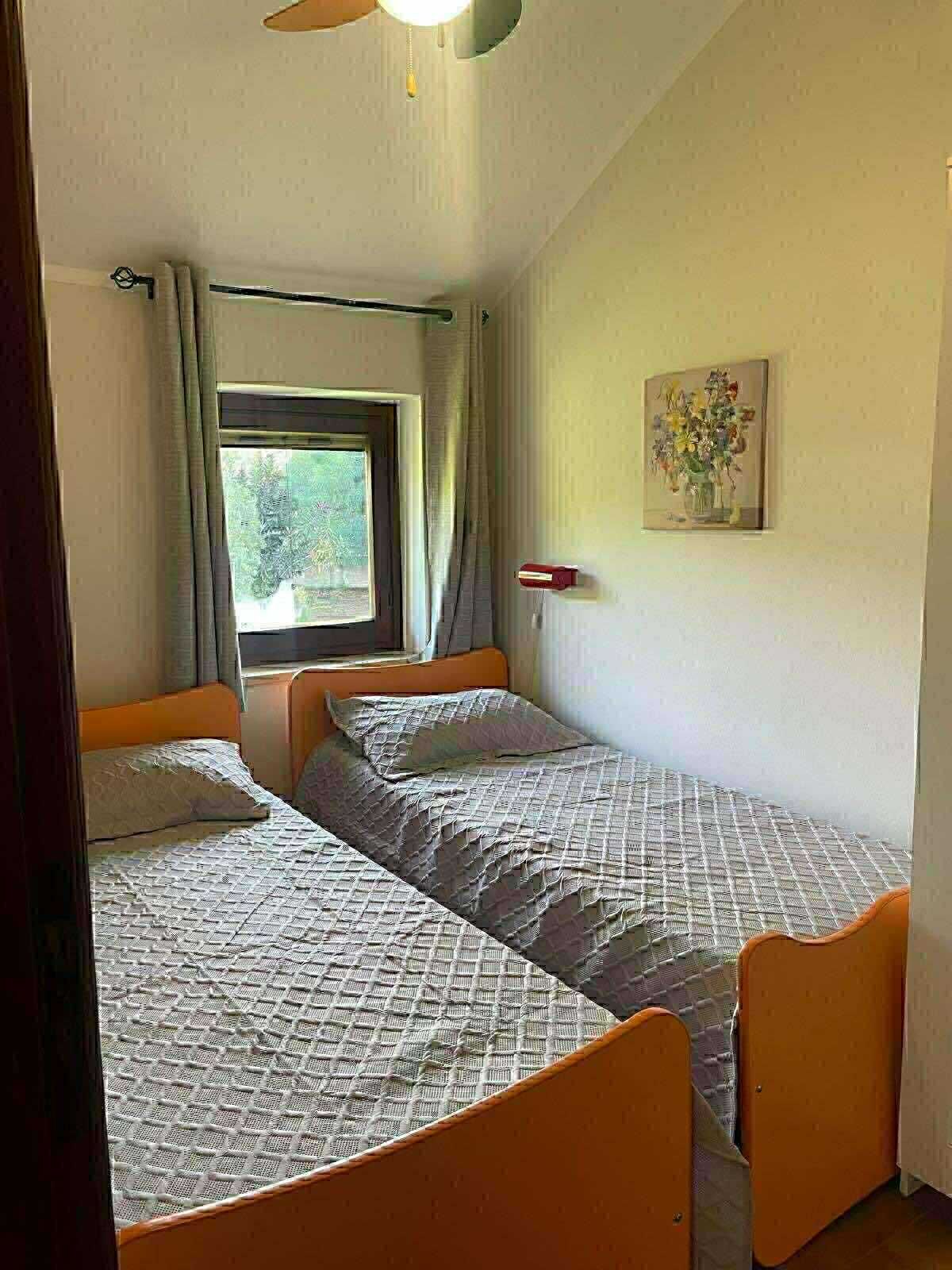 Une chambre avec deux lits, une fenêtre avec des rideaux, un luminaire fixé au mur et un tableau.