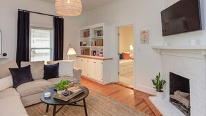 Un salon moderne avec un canapé, une table basse et une cheminée. On y trouve également une bibliothèque et un téléviseur fixé au mur.