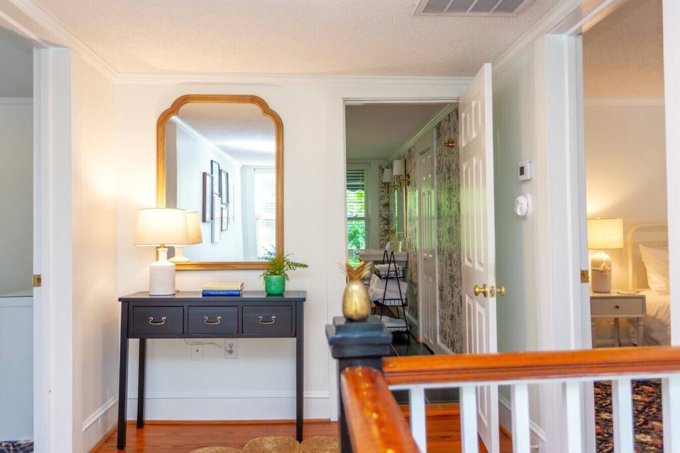 A hallway with a dark console table, a mirror, and a lamp. There is a door leading to another room.