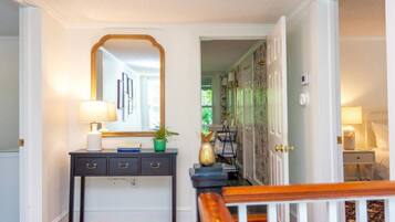 A hallway with a dark console table, a mirror, and a lamp. There is a door leading to another room.