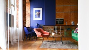 Ein modernes Wohnzimmer mit Fischgrätparkett, einem roten Sessel, einem grünen Sofa und einer Vitrine mit Geschirr.