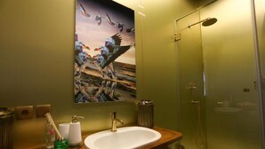 Ein Badezimmer mit einem Holzkosmetikschrank, einem weißen Waschbecken, einer Duschkabine aus Glas und einem Vogelgemälde an der Wand.