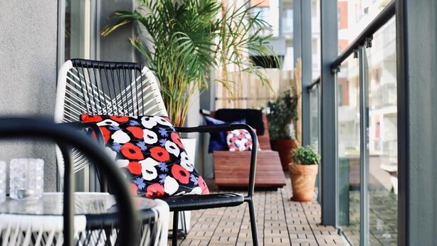 Ein Balkon mit Stuhl und Tisch, Topfpflanzen und Blick auf Gebäude.