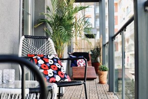 A balcony with a chair and table, potted plants, and a view of buildings.