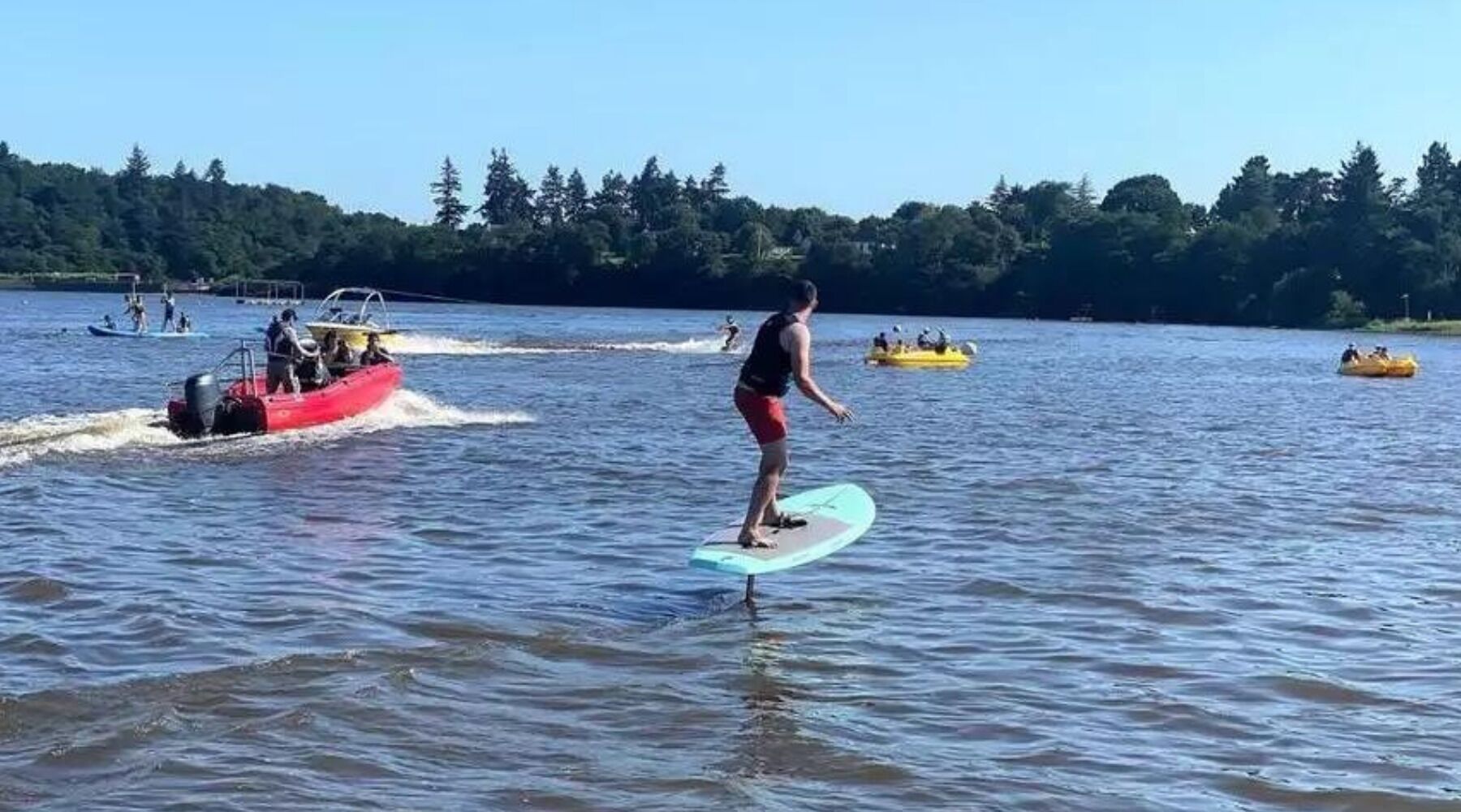 A person surfing on a calm lake with boats and rafts in the background.