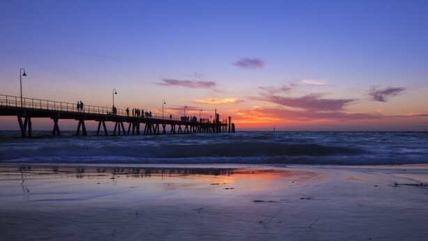 Een steiger die zich uitstrekt in de oceaan bij zonsondergang, met mensen die erover lopen.