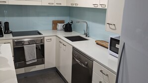 Een moderne keuken met witte kastjes, een zwarte vaatwasser, een witte koelkast en een dubbele spoelbak.