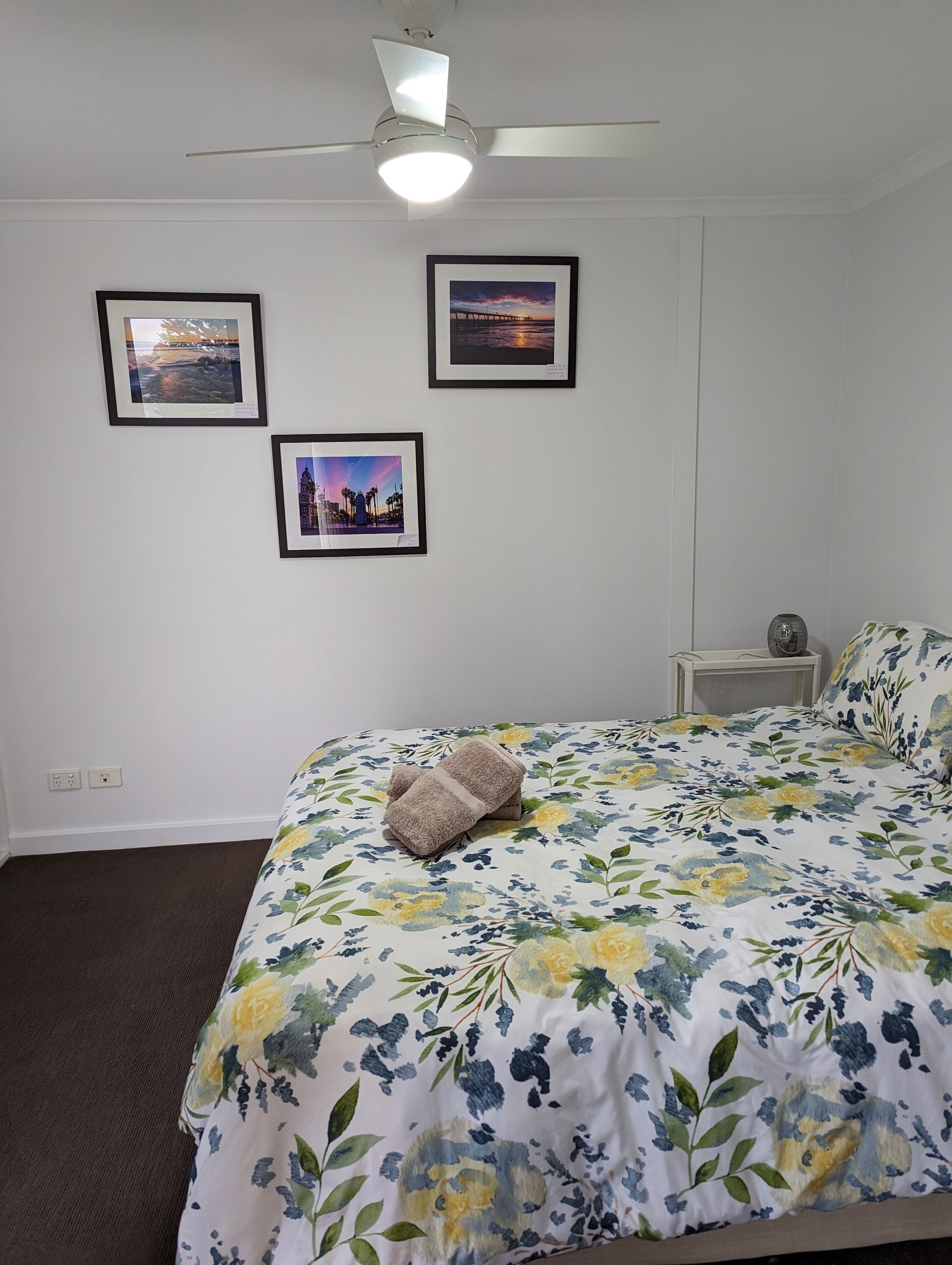 Une chambre à coucher avec un lit, un ventilateur de plafond et trois tableaux encadrés accrochés au mur.