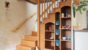 A wooden staircase with built-in shelves, a small statue, and a kitchen area with a refrigerator and a plant. - A cosy riverside cottage in the Devon countryside on the Edge of Dartmoor. (Yelverton)