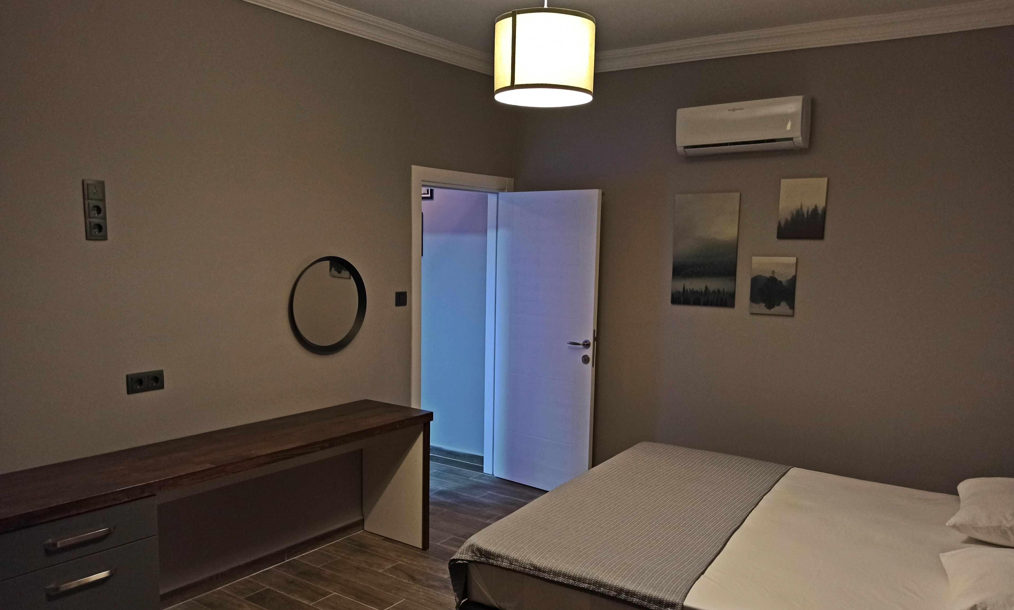 A hotel room with a bed, a bedside table, a mirror, an air conditioning unit, and a door leading to another room.