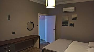 A hotel room with a bed, a bedside table, a mirror, an air conditioning unit, and a door leading to another room.