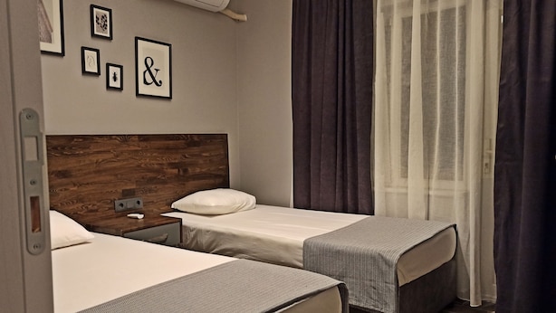 A hotel room with two beds, a wooden headboard, a wall-mounted air conditioner, and a window with dark curtains. - Merve Apart Otel (Alanya)