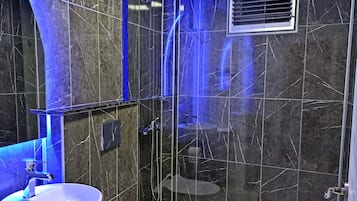 Een moderne badkamer met een groot wit wastafelmeubel, een douche met glazen deur en donkere marmeren wanden.