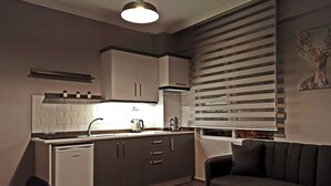 A compact kitchen with a dishwasher, white cabinets, a black countertop, and a window with blinds. - Merve Apart Otel (Alanya)