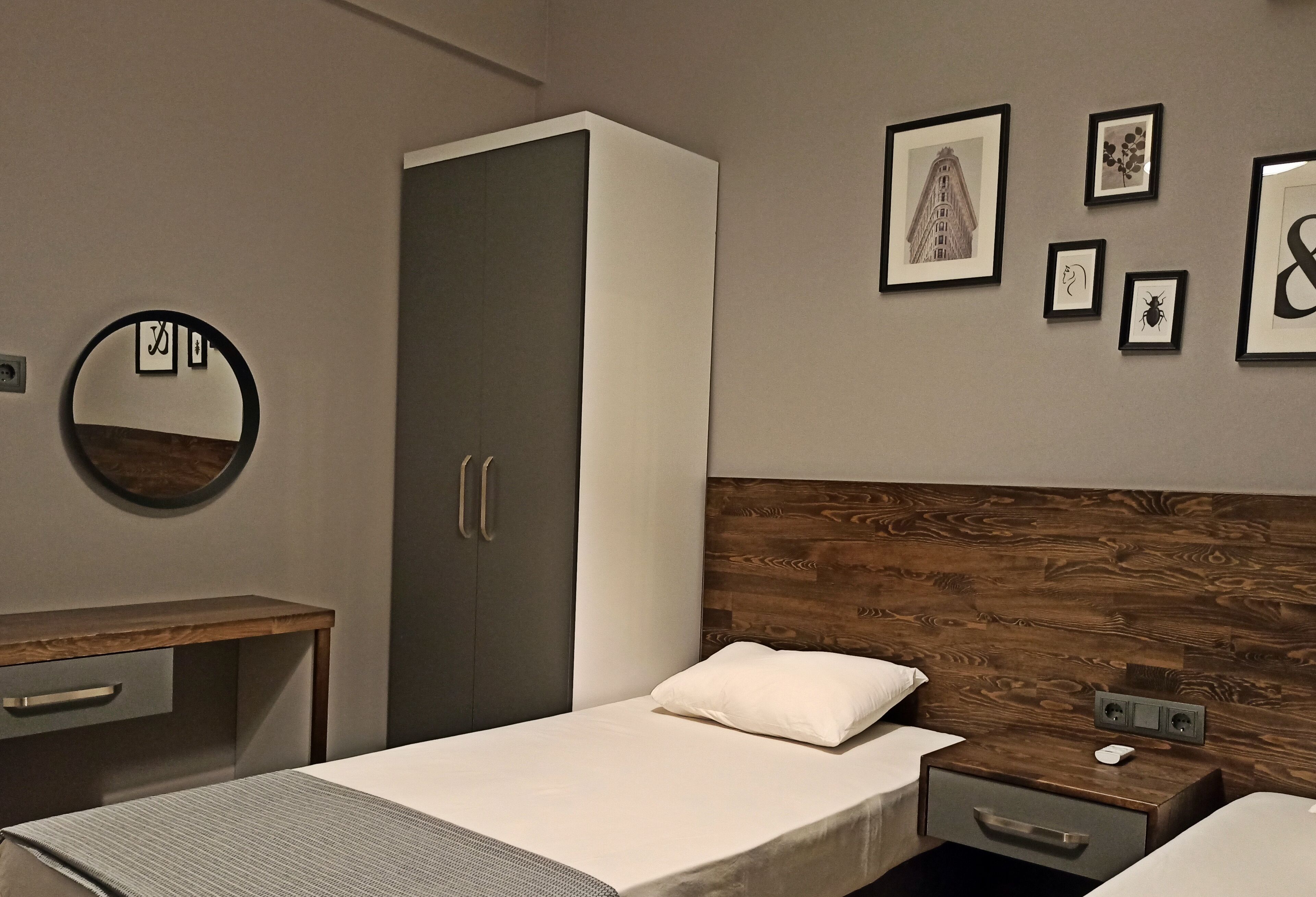 Een moderne slaapkamer met een houten hoofdbord, een bed met een wit kussen, een nachtkastje, een kledingkast en ingelijste foto's aan de muur.