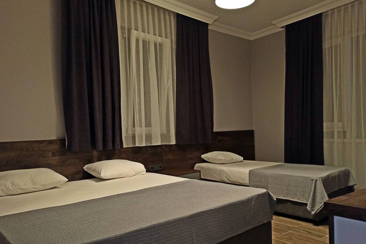 A hotel room with two single beds, a wooden headboard, a small desk, and a window with curtains.