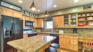 Eine moderne Küche mit Granit Arbeitsplatten, Holzschränken, einem Edelstahl-Kühlschrank, einer Mikrowelle und einer Kaffeemaschine.