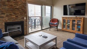 Ein Wohnzimmer mit Kamin, Fernseher und einer Schiebetür zu einem Balkon.