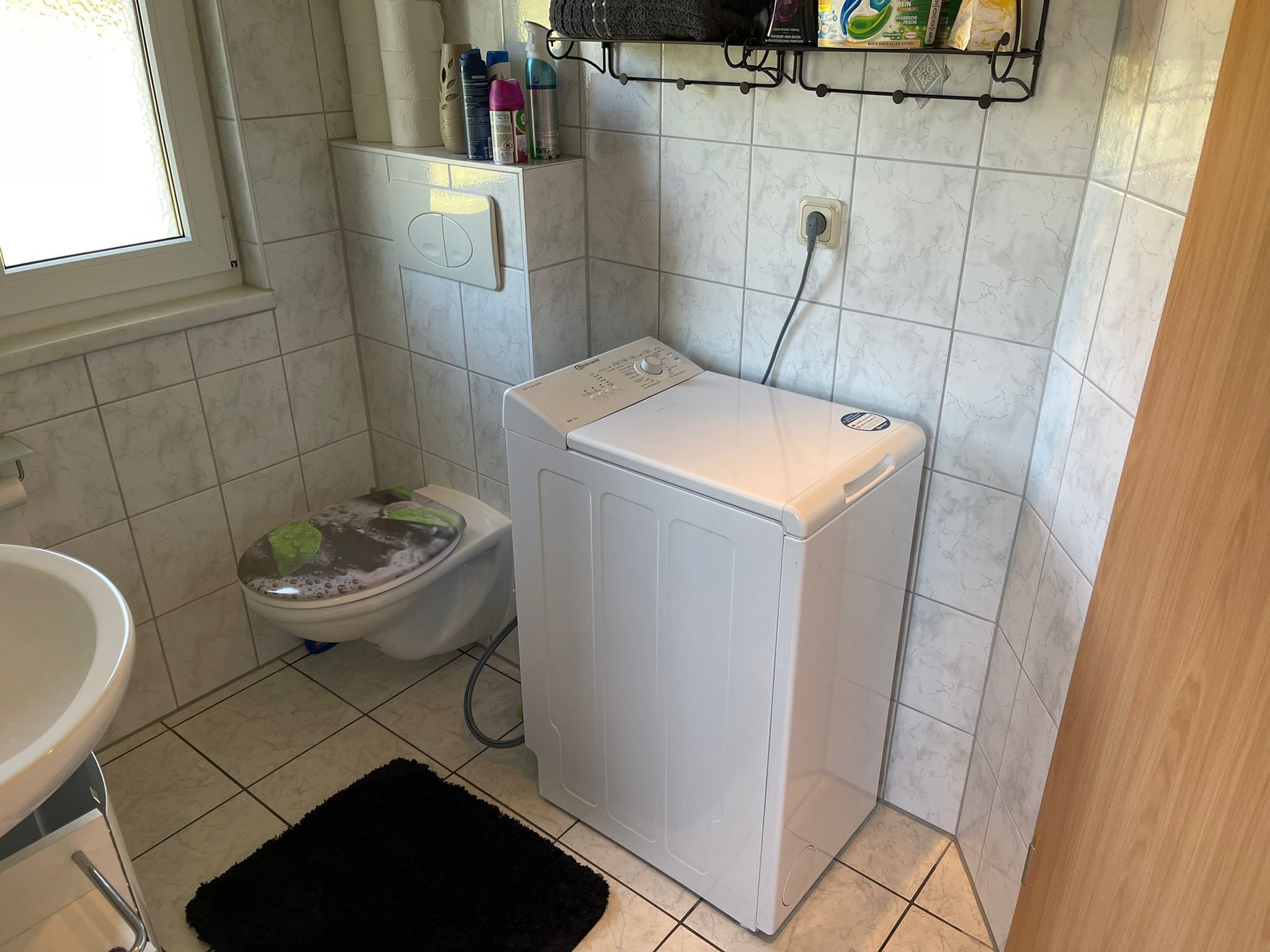 Ein kleines Badezimmer mit Toilette, Waschmaschine und Ablagefläche für Pflegeartikel.