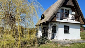 A traditional house with a thatched roof, a balcony, and a small garden area. - Hobbithaus resort (Eggesin)