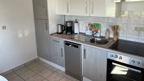 A compact kitchen with white cabinets, a stainless steel dishwasher, a coffee maker, and a toaster. - Hobbithaus resort (Eggesin)