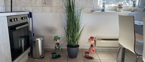 A kitchen with a stove, trash can, potted plants, and decorative figurines.