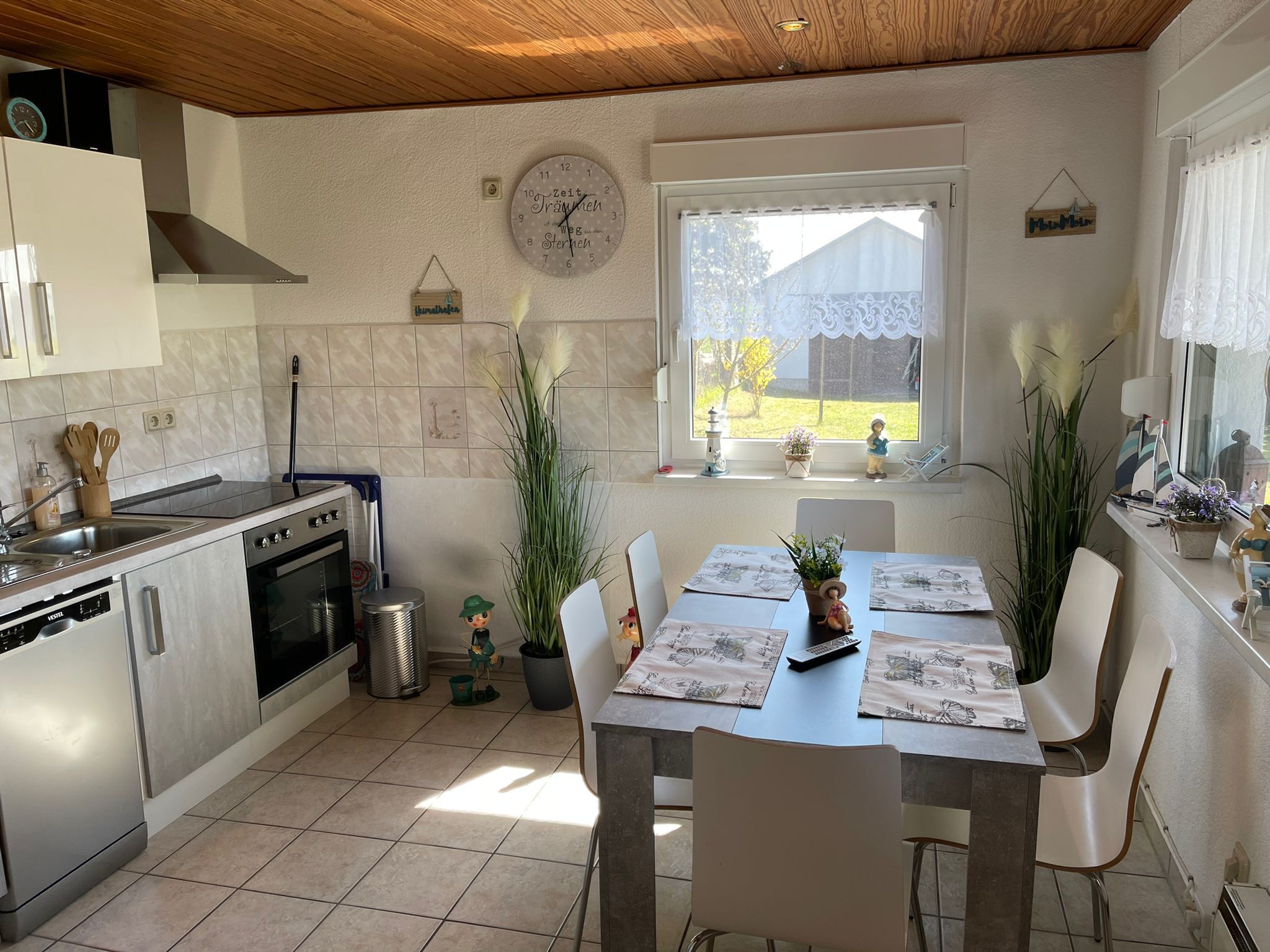 Een moderne keuken met een eethoek, met een klok, potplanten en uitzicht op het groen.