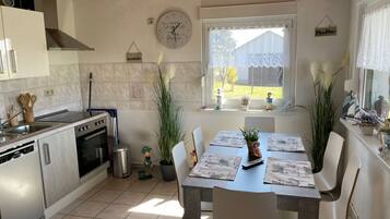 Een moderne keuken met een eethoek, met een klok, potplanten en uitzicht op het groen.