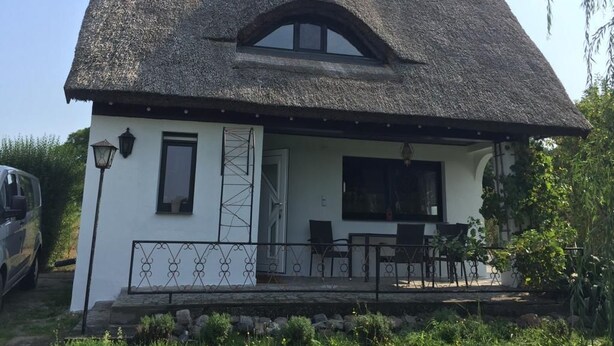 A white house with a thatched roof, a small porch with a table and chairs, and a car parked in the driveway. - Hobbithaus resort (Eggesin)