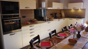 A modern kitchen with built-in appliances, wooden cabinets, and a dining area set for a meal. - Gîte les Meulots, isolated in the Morvan nature park (Blanot)
