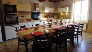 A modern kitchen with built-in appliances, a dining area with a long table set for six, and a large window providing natural light. - Gîte les Meulots, isolated in the Morvan nature park (Blanot)