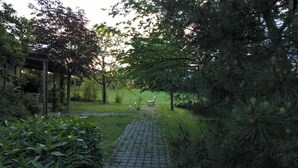 A paved pathway leading through a garden with a wooden pergola and benches.