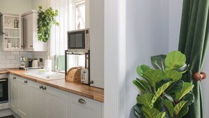 Et køkken med hvide skabe, en træbordplade, en mikroovn, en brødrister og en potteplante.